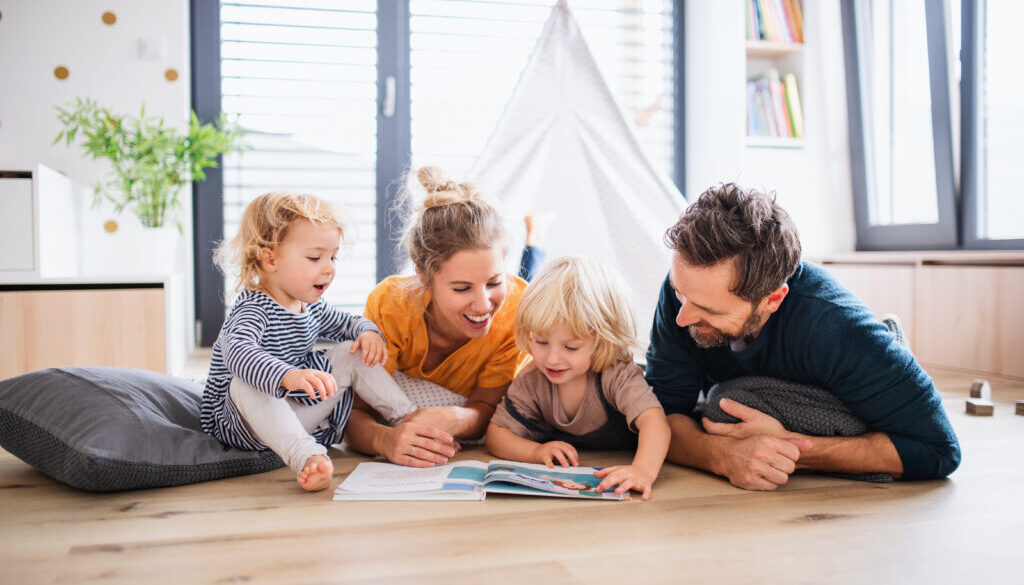 Mother, father, and two young kids reading a book on the floor of their home set at the perfect temperature thanks to a great HVAC system