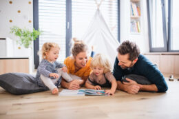 Mother, father, and two young kids reading a book on the floor of their home set at the perfect temperature thanks to a great HVAC system
