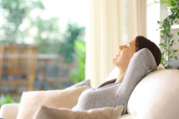 Young woman sitting on her couch, breathing deeply and enjoying the quality of the air in her home thanks to following the tips in this blog